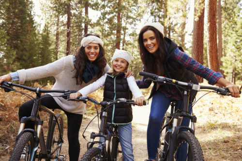 Female parents cycling with their daughter in a forest